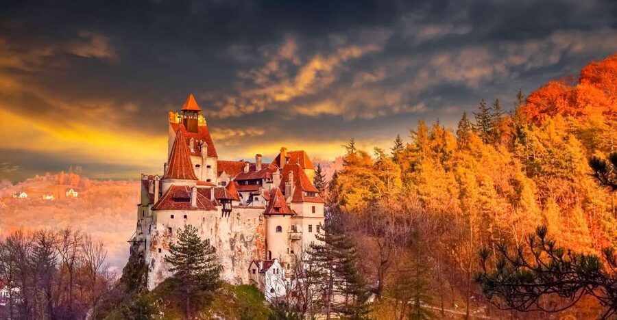 Bran Castle on its crag at dusk, autumn woods below